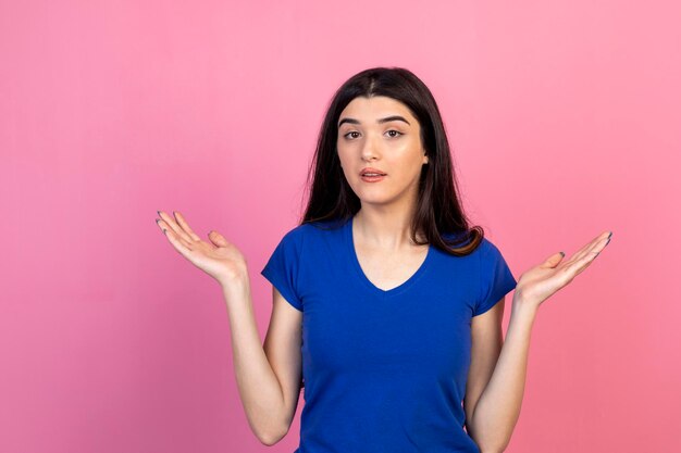 Jonge vrouw die op een roze achtergrond staat en haar handen wijd open houdt Foto van hoge kwaliteit