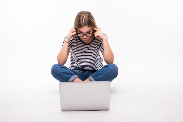 Jonge vrouw die op laptop op de vloer over witte muur werkt