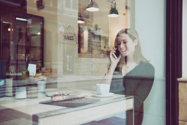 Jonge vrouw die op telefoon in aardige koffie spreekt