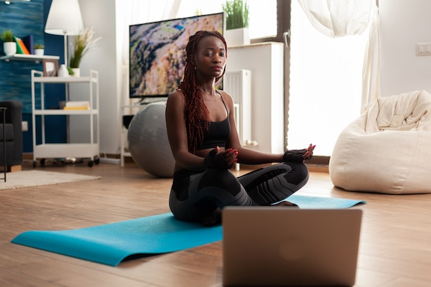 Jonge vrouw die op yogamat zit en kalme harmonie beoefent en zen mediteert voor een gezonde levensstijl, ontspannen in lotushouding