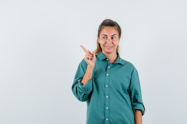 Jonge vrouw die opzij in blauw overhemd wijst en blij kijkt