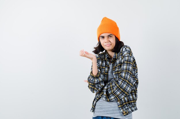 Jonge vrouw die palm in oranje hoed en geruit overhemd uitspreidt en ontevreden kijkt
