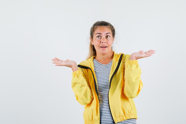 Jonge vrouw die palmen opzij in t-shirt, jasje uitspreidt en hoopvol, vooraanzicht kijkt.