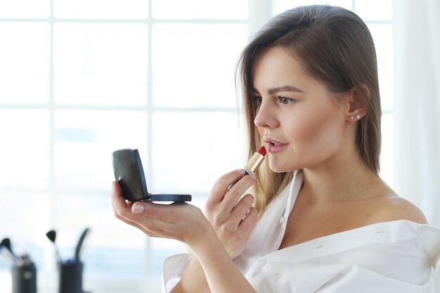 Jonge vrouw die rode lippenstift toepast.