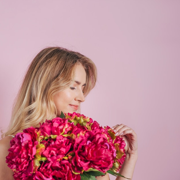 Jonge vrouw die roze boeket tegen roze achtergrond bekijkt