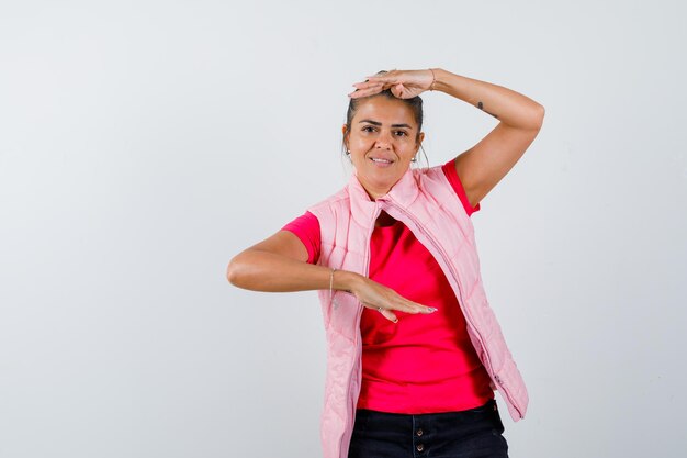 Jonge vrouw die schubben in roze t-shirt en jasje toont en gelukkig kijkt