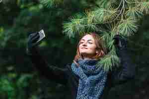 Gratis foto jonge vrouw die selfie op smartphone dichtbij naaldtakje nemen