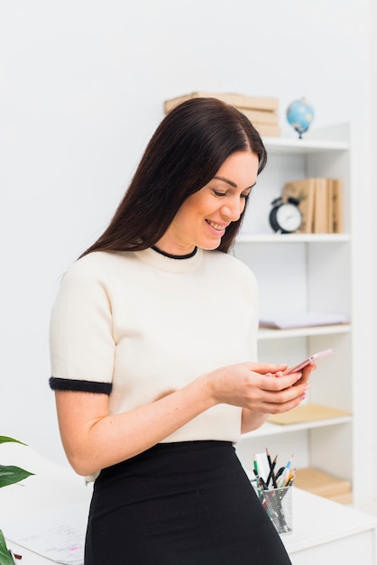 Jonge vrouw die smartphone in bureau bekijkt