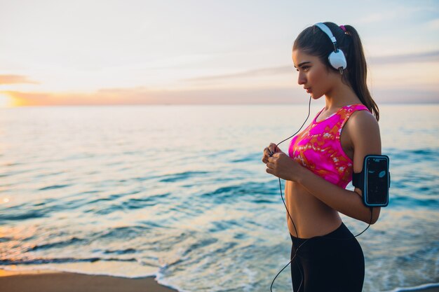 Jonge vrouw die sportoefeningen doet op zonsopgangstrand in ochtend