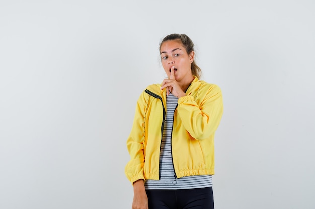 Jonge vrouw die stiltegebaar in t-shirt, jasje toont en verstandig kijkt. vooraanzicht.