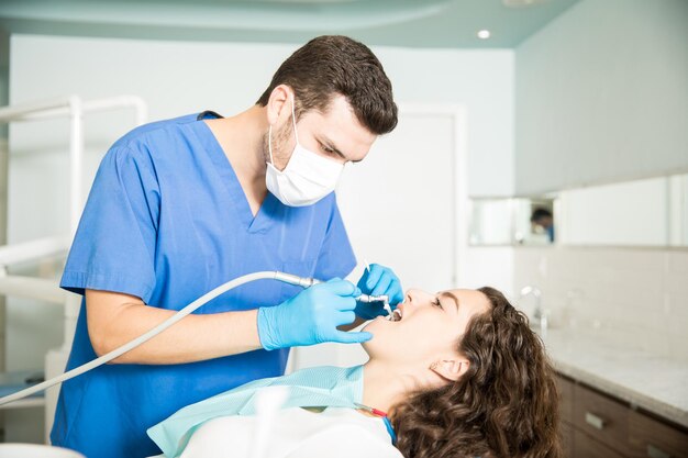 Jonge vrouw die tandheelkundige behandeling krijgt van mannelijke tandarts in kliniek