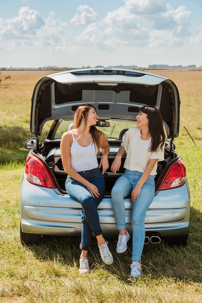 Jonge vrouw die tegen hun auto leunt