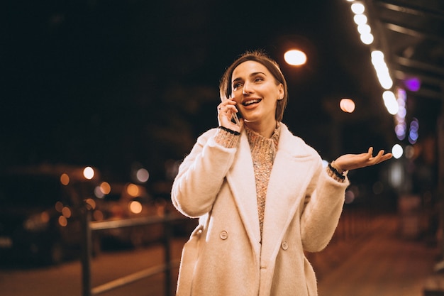 Jonge vrouw die telefoon buiten de nachtstraat met behulp van