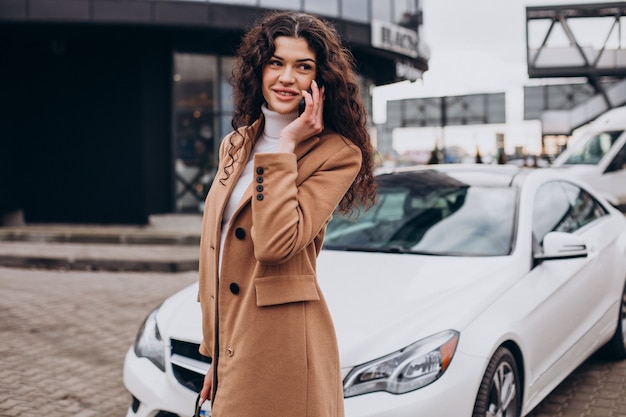 Jonge vrouw die telefoon gebruikt en bij de auto staat