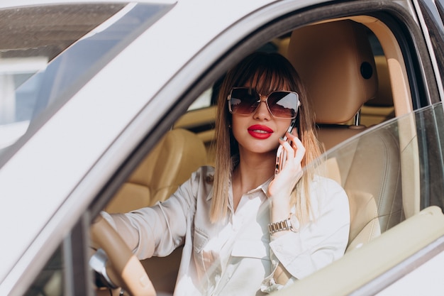 Jonge vrouw die telefoon in haar auto gebruikt