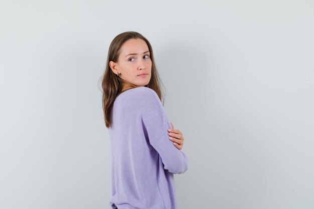 Jonge vrouw die terugkijkt terwijl ze in lila blouse poseren en er indrukwekkend uitziet. vooraanzicht.