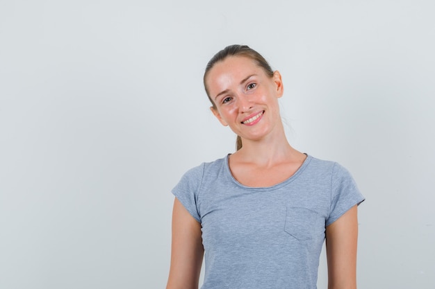 Jonge vrouw die terwijl het glimlachen in grijs t-shirt vooraanzicht kijkt.