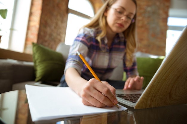 Jonge vrouw die thuis studeert tijdens online cursussen of gratis informatie door zelf notities te maken