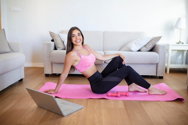 Jonge vrouw die thuis traint in een woonkamer Videoles Jonge vrouw die oefeningen herhaalt tijdens het kijken naar online trainingssessie Mooie jonge vrouw die fitnessoefening thuis doet