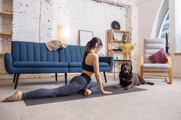 Jonge vrouw die thuis traint tijdens lockdown, yoga-oefeningen met de hond