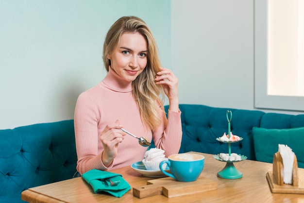 Gratis foto jonge vrouw die van de meringue en cappuccinokoffie geniet in caf�