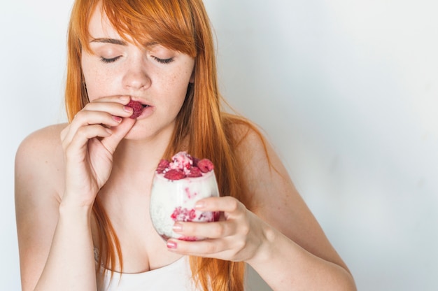 Jonge vrouw die van frambozen in yoghurt genieten smoothie op witte achtergrond