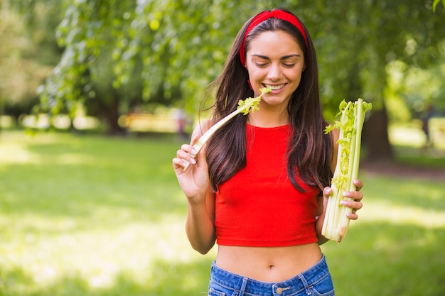 Jonge vrouw die verse selderie in het park eet