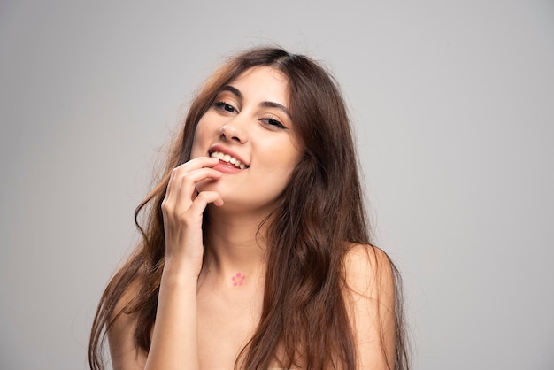 Jonge vrouw die vingers in de mond stopt op een grijze muur.