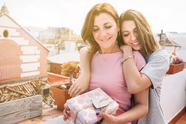 Jonge vrouw die vrouw met gift op straat omhelst