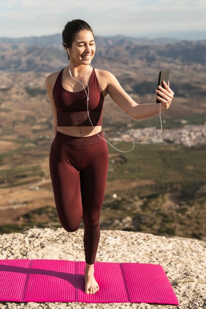 Jonge vrouw die yoga doet en telefoon met behulp van