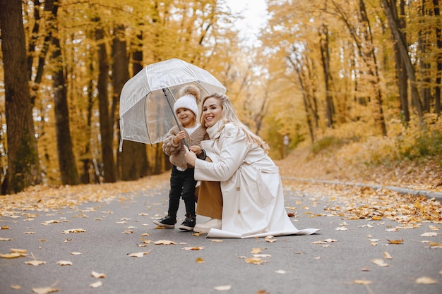 Jonge vrouw die zich in de herfstbos bevindt. blonde vrouw haar dochter knuffelen. meisje draagt beige trui en witte hoed en houdt een transparante paraplu vast.