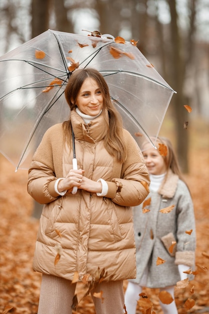Jonge vrouw die zich in de herfstbos bevindt Donkerbruine vrouw die een transparante paraplu houdt Haar dochter die erachter staat