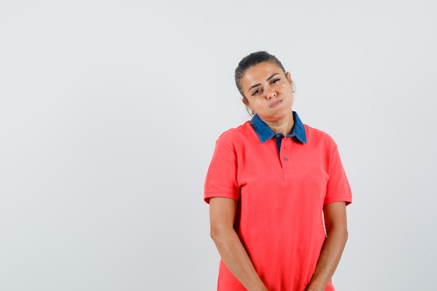 Jonge vrouw die zich rechtop bevindt, puffende wangen en voor camera in rood t-shirt stelt en mooi, vooraanzicht kijkt.