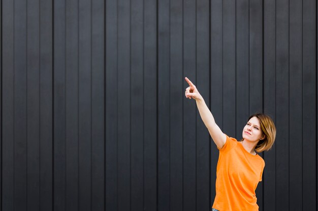 Jonge vrouw die zich tegen zwarte muur bevindt die haar vinger naar omhoog richt