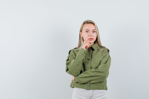 Jonge vrouw die zich voordeed als zich concentreren op iets in een groene jas en er mooi uitziet, vooraanzicht.