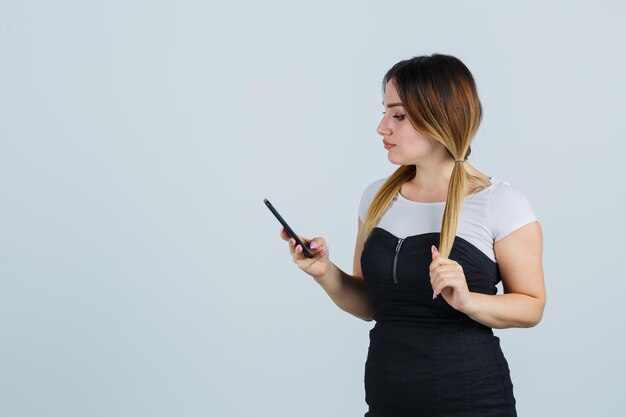 Jonge vrouw die zich voordeed terwijl ze haar haar schikt en haar mobiele telefoon vasthoudt