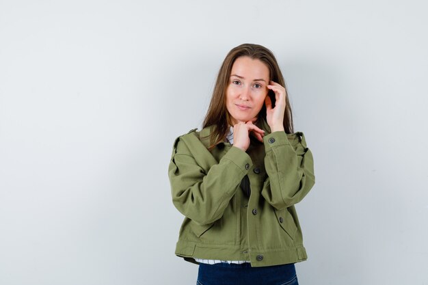 Jonge vrouw die zich voordeed terwijl ze in shirt, jas denkt en er gracieus uitziet, vooraanzicht.