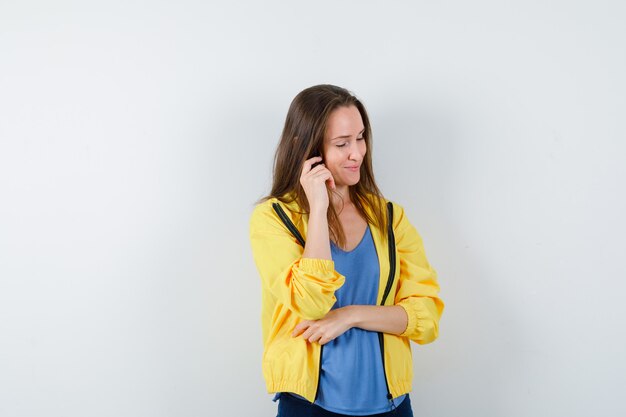 Jonge vrouw die zich voordeed terwijl ze in t-shirt, jas denkt en er optimistisch uitziet. vooraanzicht.