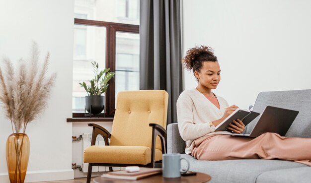 Jonge vrouw die zittend op de bank werkt