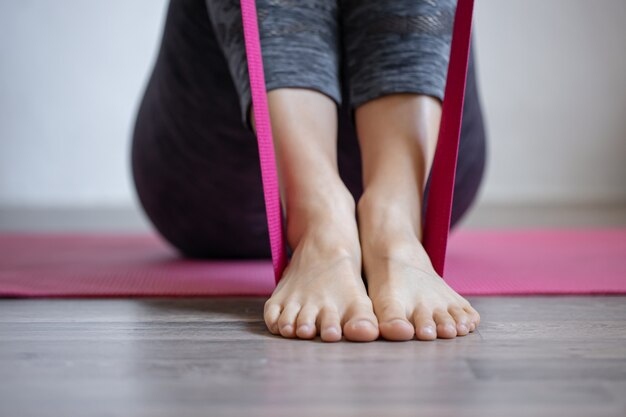 Jonge vrouw doet sportoefeningen met elastische band thuis op de mat, fitness thuis, stretching en yoga.