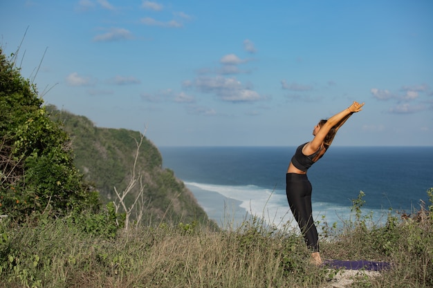 Jonge vrouw doet yoga buitenshuis met geweldig achteraanzicht. Bali. Indonesië.