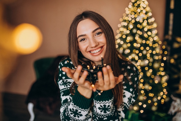 Jonge vrouw door de kerstboom met Kerstmis gloeiende lichten
