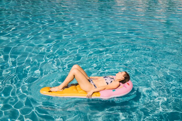Jonge vrouw drijvend op opblaasbare matras in het zwembad
