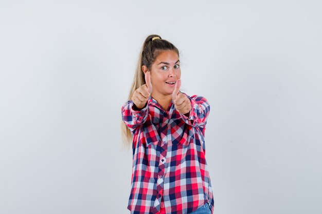 Jonge vrouw dubbele duimen opdagen in casual shirt en gelukkig kijken. vooraanzicht.