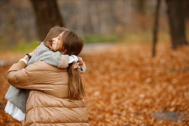 Jonge vrouw en klein meisje in het herfstbos Vrouw en haar dochter knuffelen Meisje draagt een grijze modejurk met een jasje