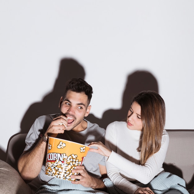 Gratis foto jonge vrouw en man die op tv let en popcorn op sofa eet