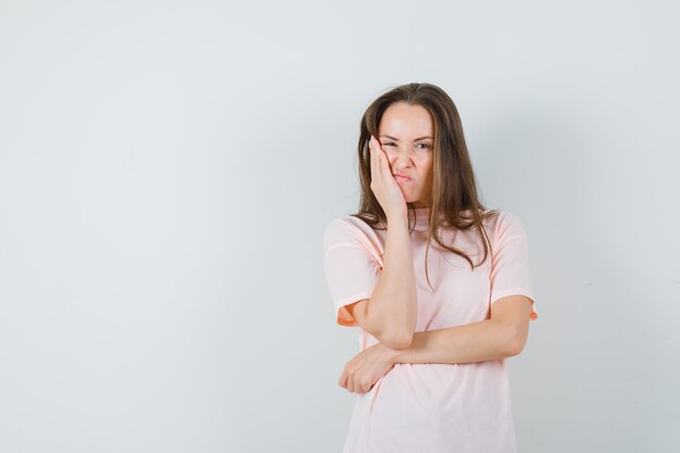 Jonge vrouw fronsend terwijl leunend wang op opgeheven palm in roze t-shirt vooraanzicht.