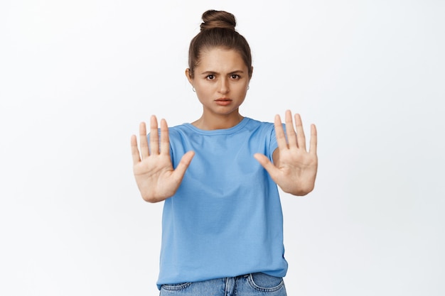 Gratis foto jonge vrouw gebaren stop, nee zeggen, handen uitstrekken om iets slechts te verbieden, staande op wit