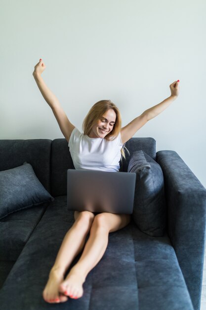 Jonge vrouw gebruikend laptop terwijl opheffend hand en thuis zittend op de laag