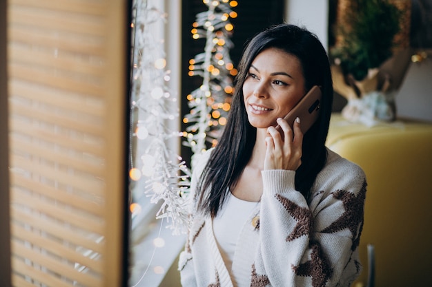 Jonge vrouw gebruikend telefoon en zich bevindt bij het venster